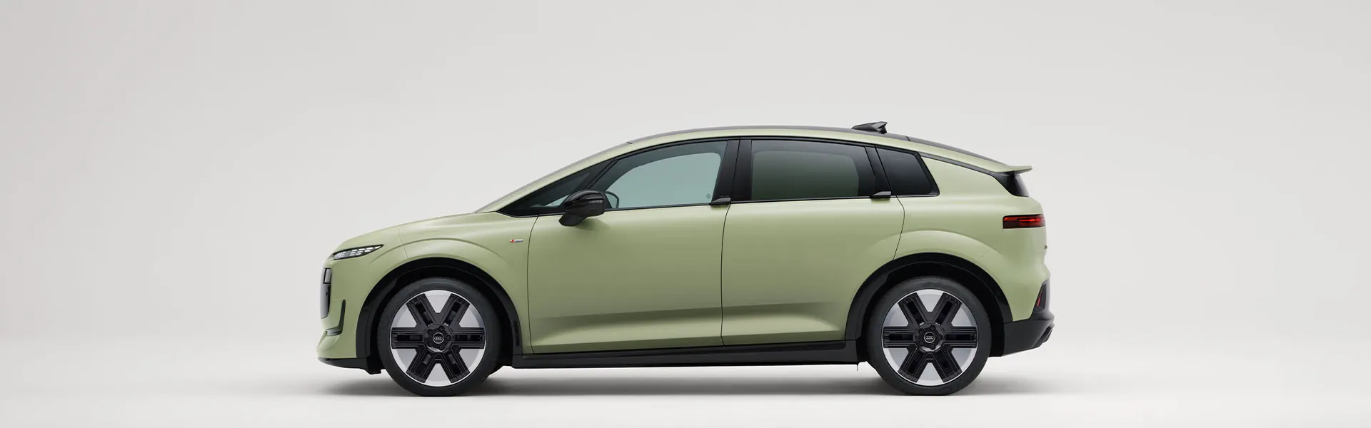 Audi A2 elétrico compacto, visto de lado, num fundo branco. O veículo é de cor verde-clara fosca, com linhas suaves.  