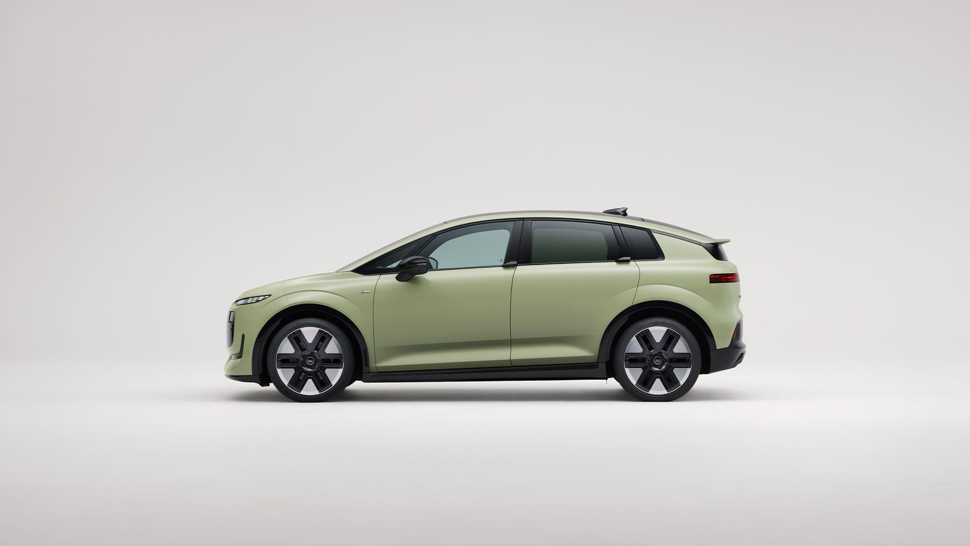 Audi A2 elétrico compacto, visto de lado, num fundo branco. O veículo é de cor verde-clara fosca, com linhas suaves.  