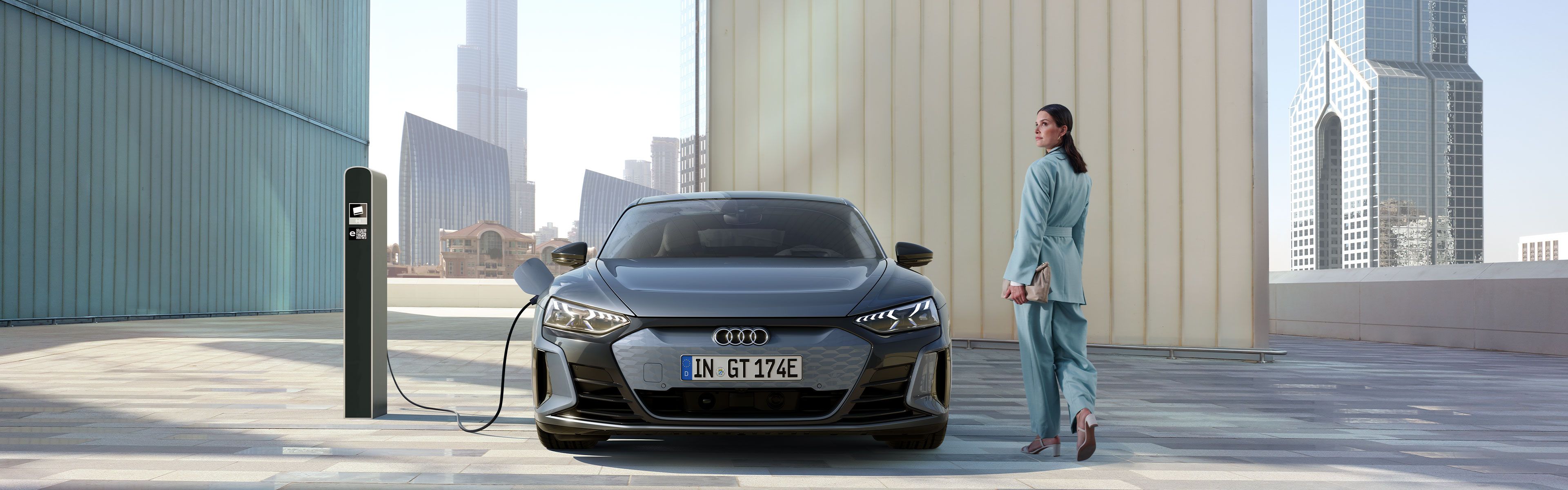 Senhora de costas ao lado de um Audi a carregar