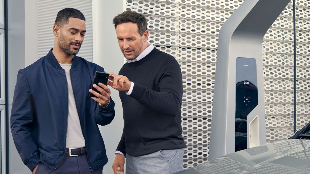Dois senhores a olhar para um telemóvel enquanto um Audi carrega