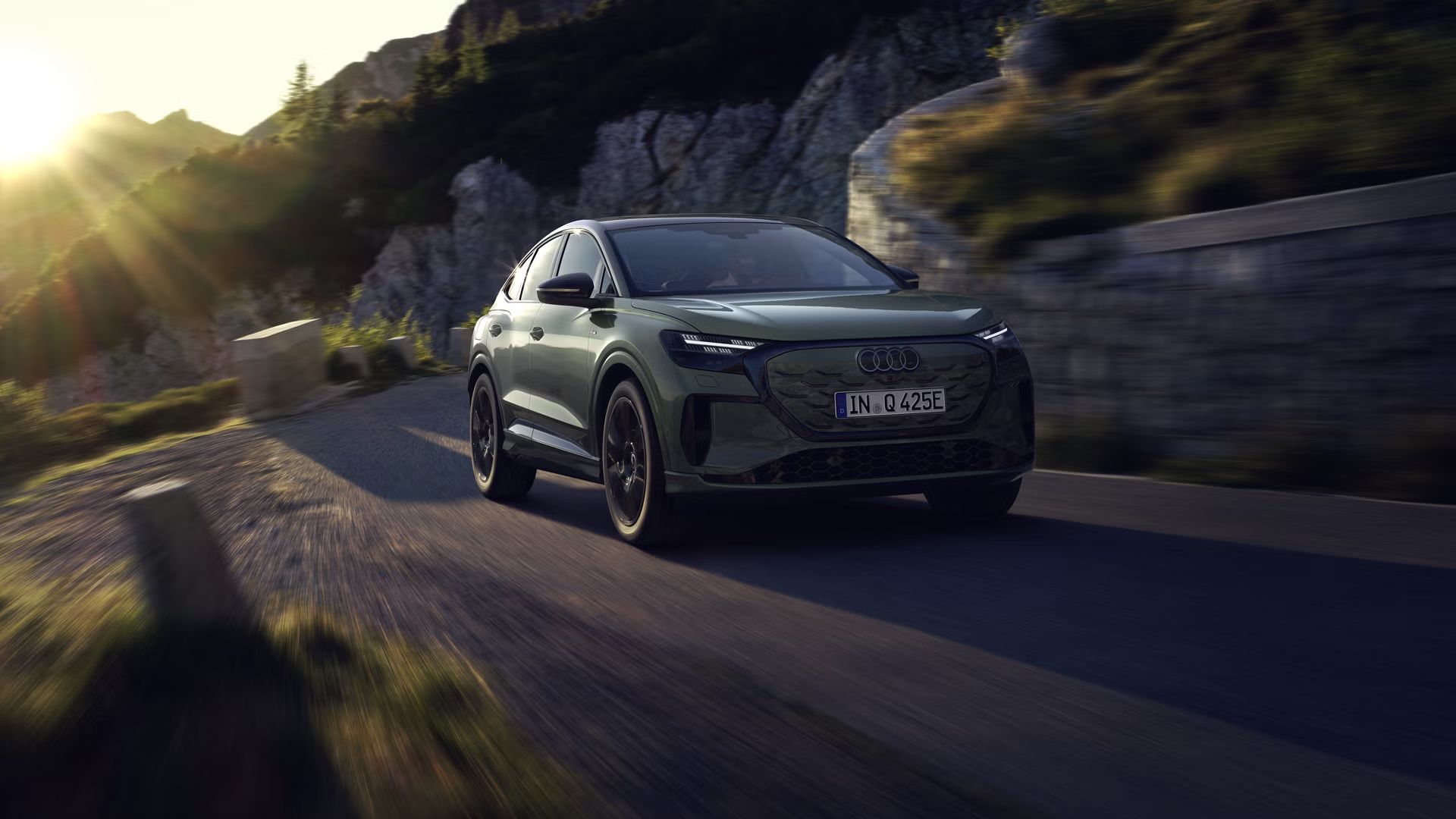 Der Q4 Sportback e-tron bei der Fahrt auf einer Bergstraße. Sonnenstrahlen von links oben beleuchten das Bild, das Fahrzeug wirft Schatten nach vorne.