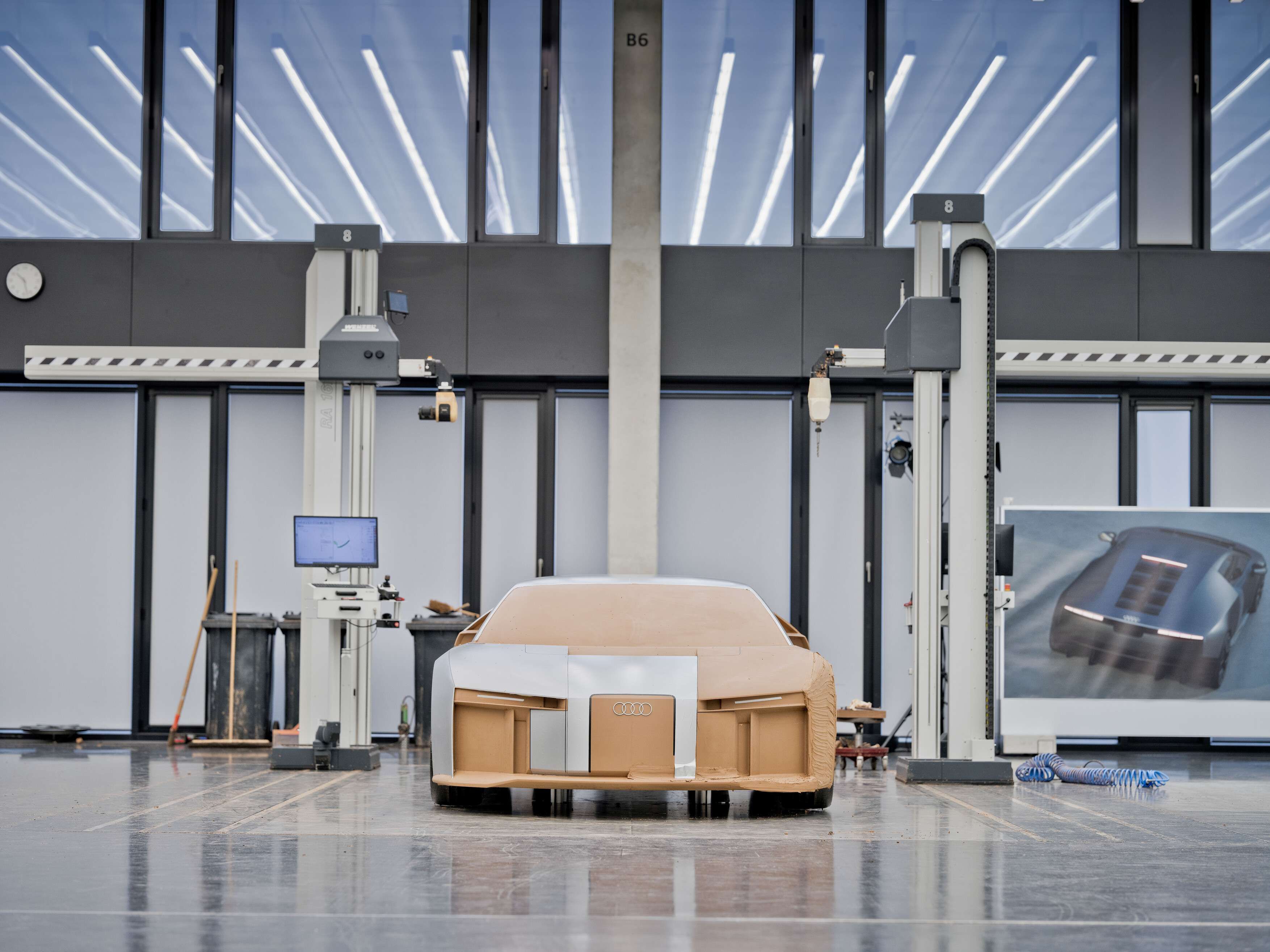 Audi Nuvolari posicionado no centro de um grande estúdio de design automóvel. Duas máquinas de medição ou fresagem verticais ladeiam o modelo, com um computador à esquerda exibindo dados técnicos. 