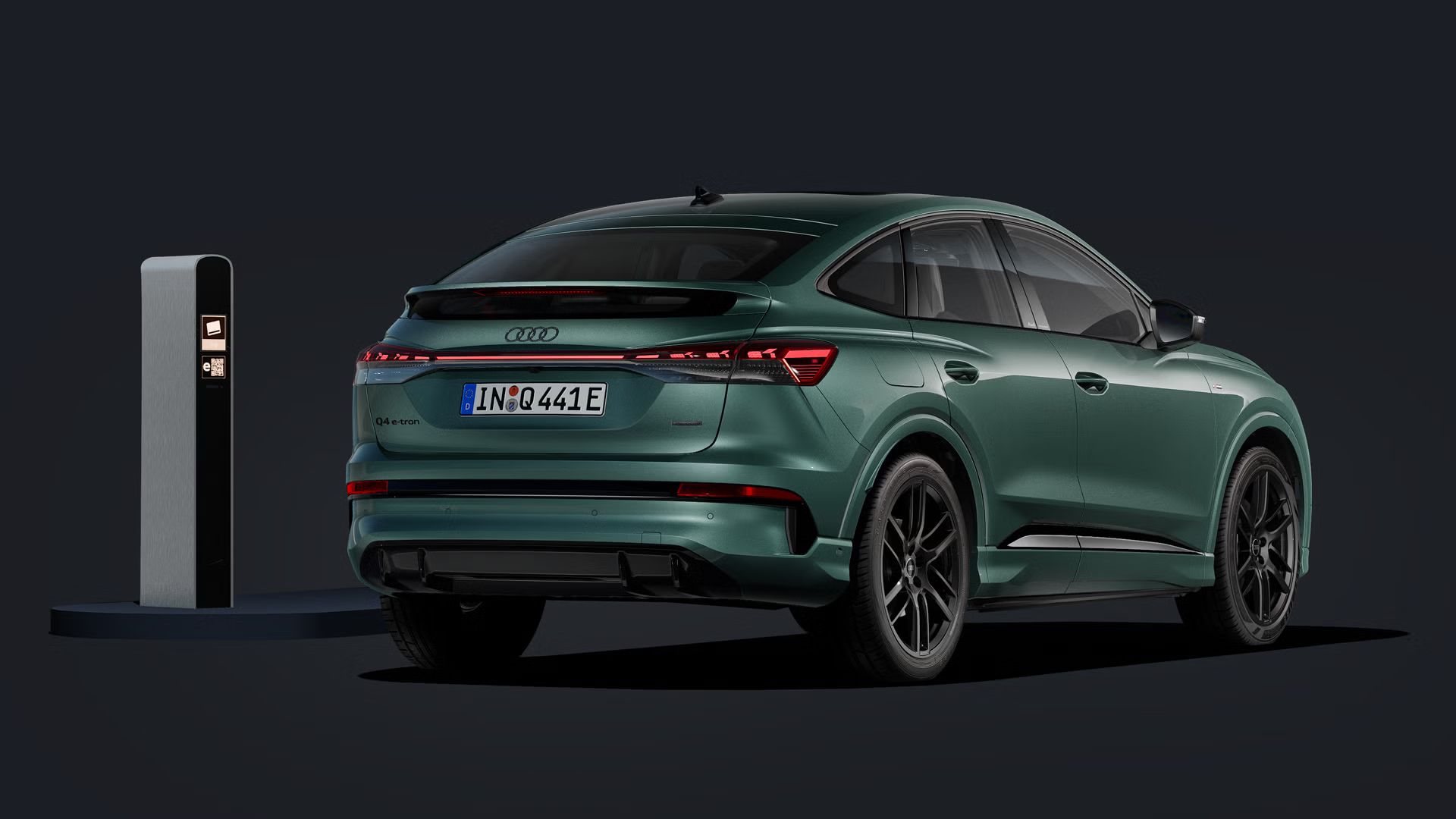 Der Q4 Sportback e-tron von schräg hinten auf dunklem Hintergrund, links daneben eine Ladesäule.